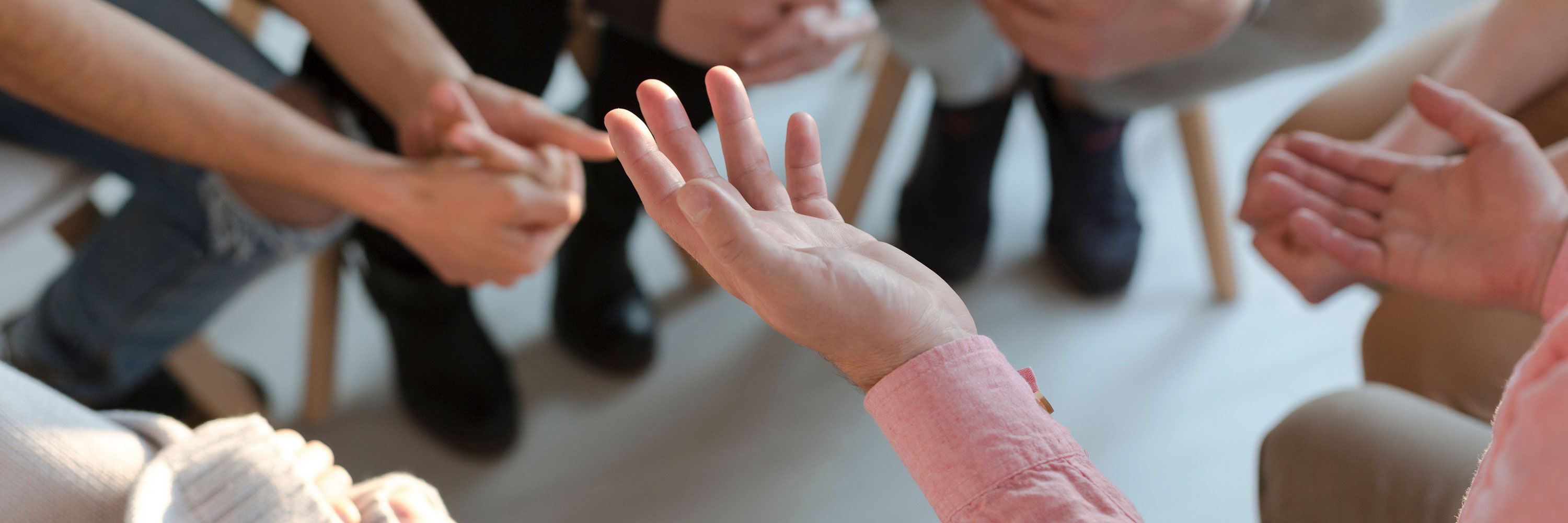 Das Bild zeigt mehrere Hände und Füße von Personen, die an einem Beratungsgespräch teilnehmen. Die Szene deutet darauf hin, dass es sich um eine Sitzung mit mehreren Klient*innen handelt.